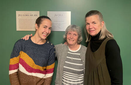 Jill Lord, MS, RN, with two others standing in front of the plaque in her honor on the conference room wall