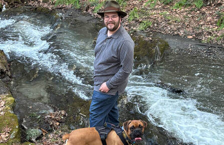 Ben Anderson standing by stream with his dog.
