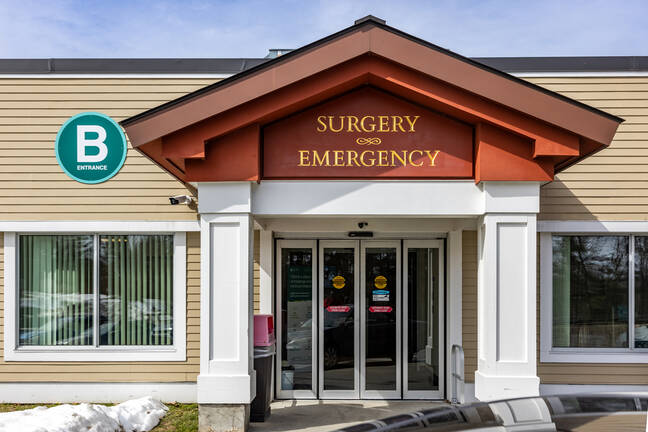 Mt. Ascutney Hospital entrance labeled “EMERGENCY,” with a red roof pediment, white columns, glass doors, and a green “B Entrance” sign